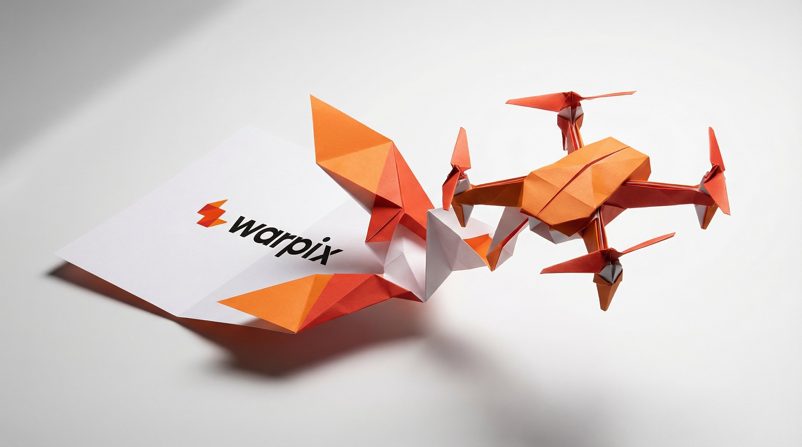 An orange and white origami drone and other geometric paper shapes are arranged around a piece of paper displaying the black 'warpix' logo with an orange 'w' symbol. This image represents Warpix, an online distributor of cutting-edge technology products, including advanced robotics and drones, symbolizing innovation and future tech.