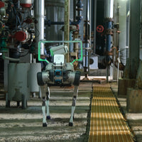 A DEEP Robotics X30 Pro quadruped robot performs an autonomous industrial inspection in a facility, equipped with an HD camera and an acoustic camera (white square with dots) for detecting leaks and anomalies. The robot navigates a complex environment with pipes and machinery, demonstrating its advanced multi-sensor fusion for real-time monitoring and predictive maintenance in hazardous conditions.